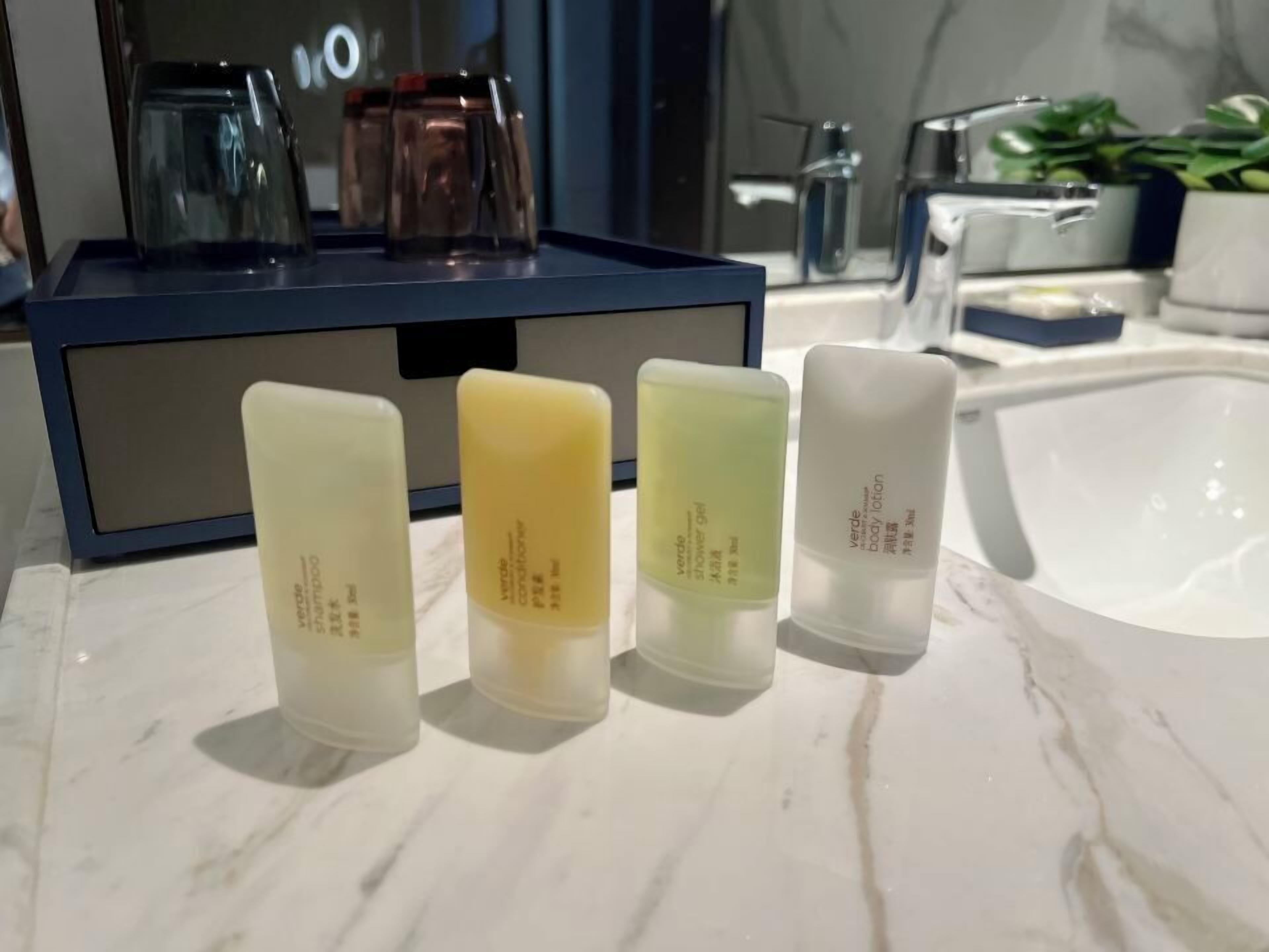 Une salle de bain avec un comptoir en marbre, une boîte de rangement bleue et quatre bouteilles de lotion pour le corps.