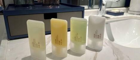 Une salle de bain avec un comptoir en marbre, une boîte de rangement bleue et quatre bouteilles de lotion pour le corps.