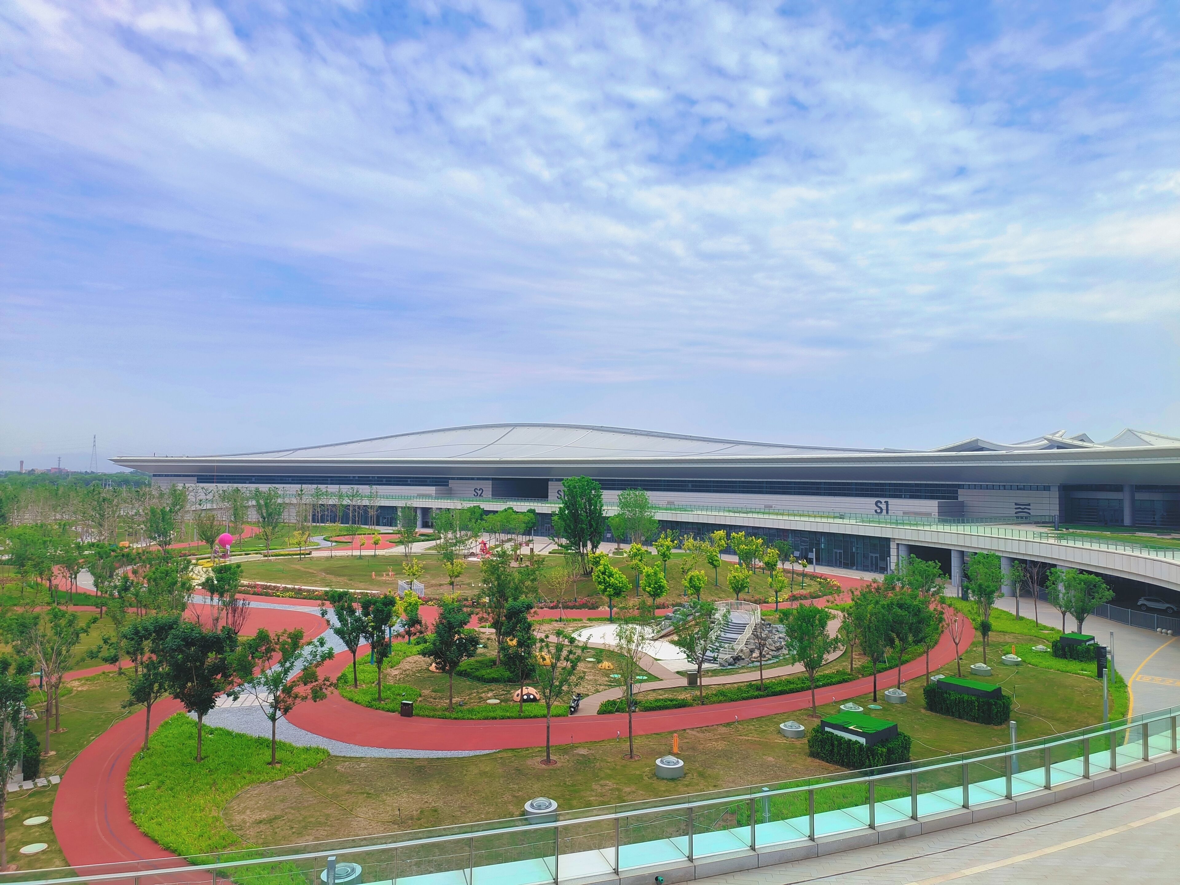 A modern building with a curved roof and a landscaped area with pathways and greenery.