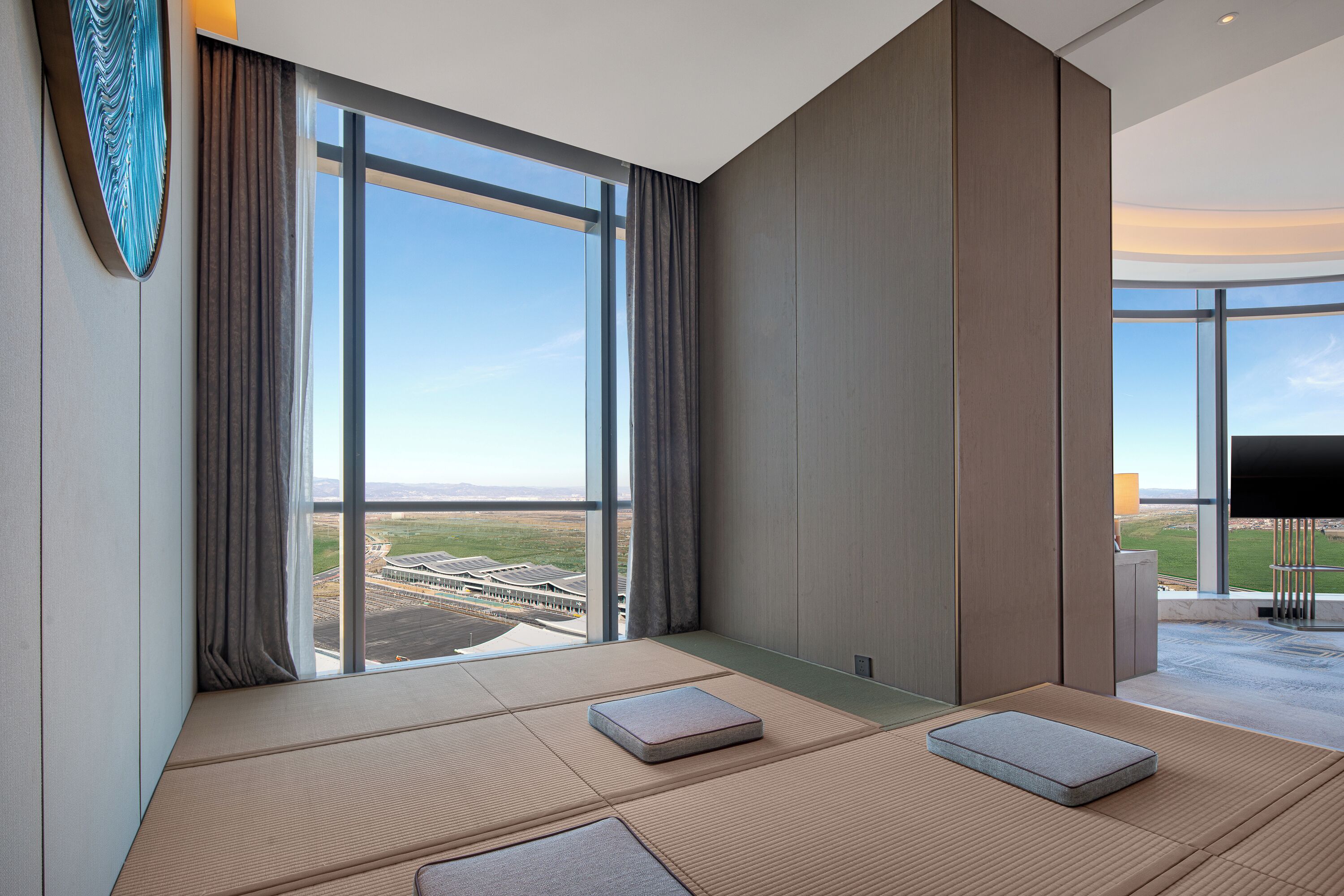 Habitación de hotel moderna con esteras de tatami, un ventanal con vistas a un edificio y una televisión de pantalla plana.