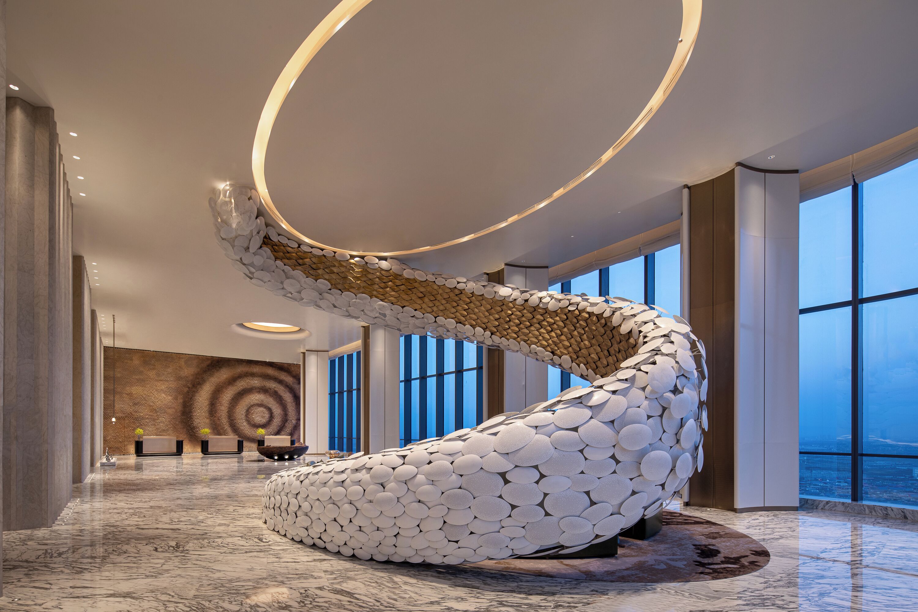 A modern lobby with a unique spiral sculpture, large windows, and a marble floor.