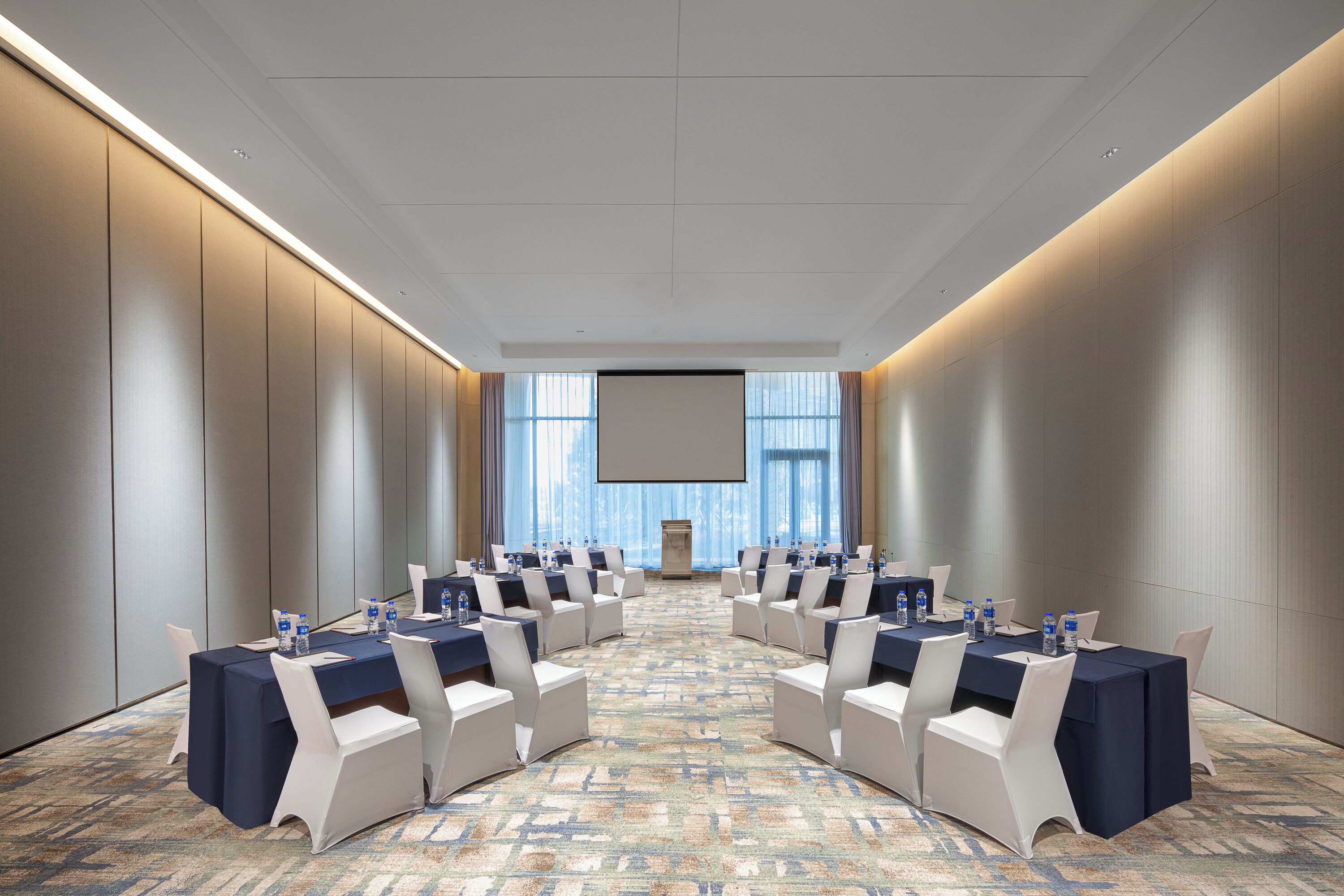 A conference room with a long table, white chairs, and a projector screen.