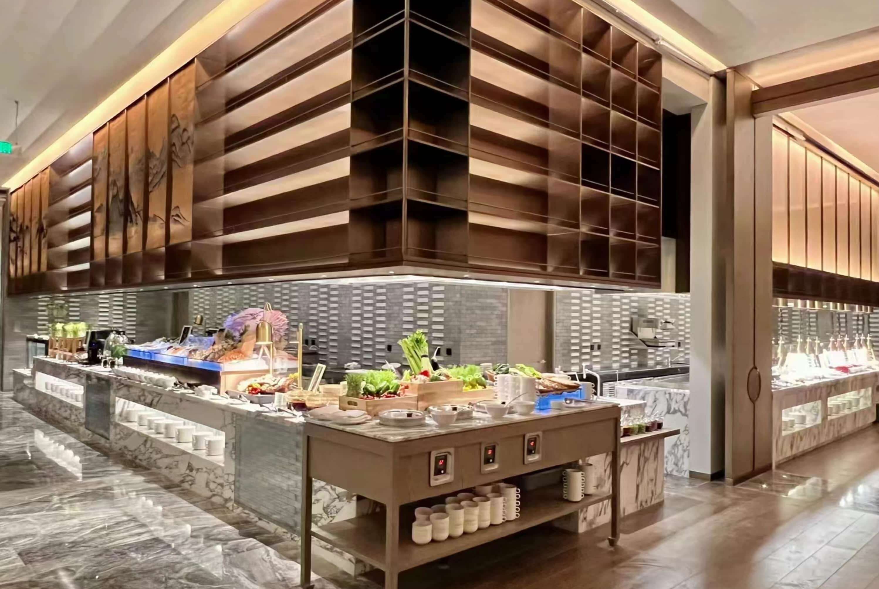 En moderne hotellobby med et marmorgulv, en receptionsdisk med et buffetbord og træpaneler på væggene.