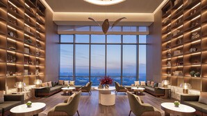 A modern lounge with a panoramic city view, featuring a central seating area with round tables and sofas, surrounded by tall bookshelves filled with decorative items. - Wyndham Shanxi Xiaohe Xincheng (Taiyuan)