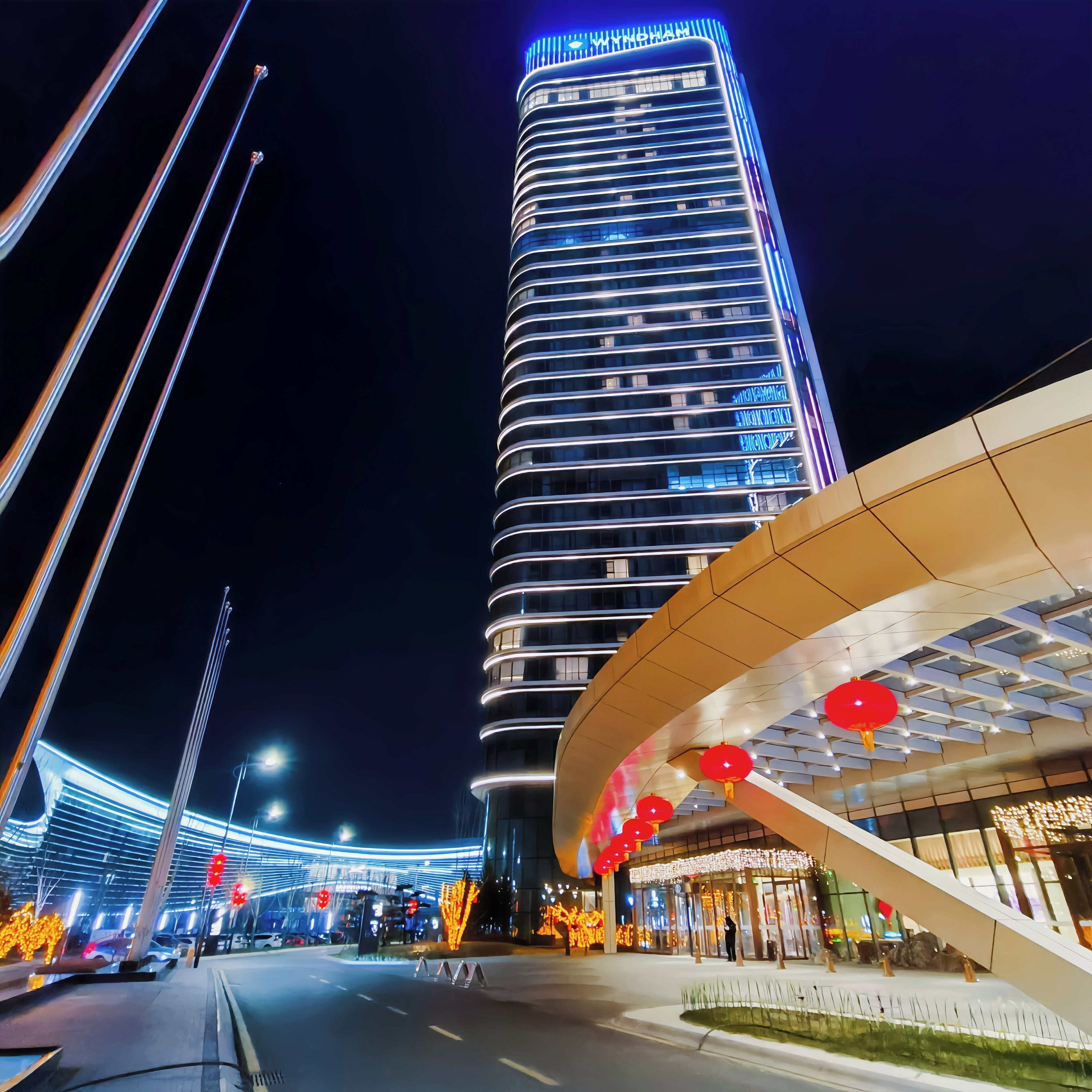 Un hotel moderno con fachada curva, señalización iluminada y una estructura vertical destacada al fondo.