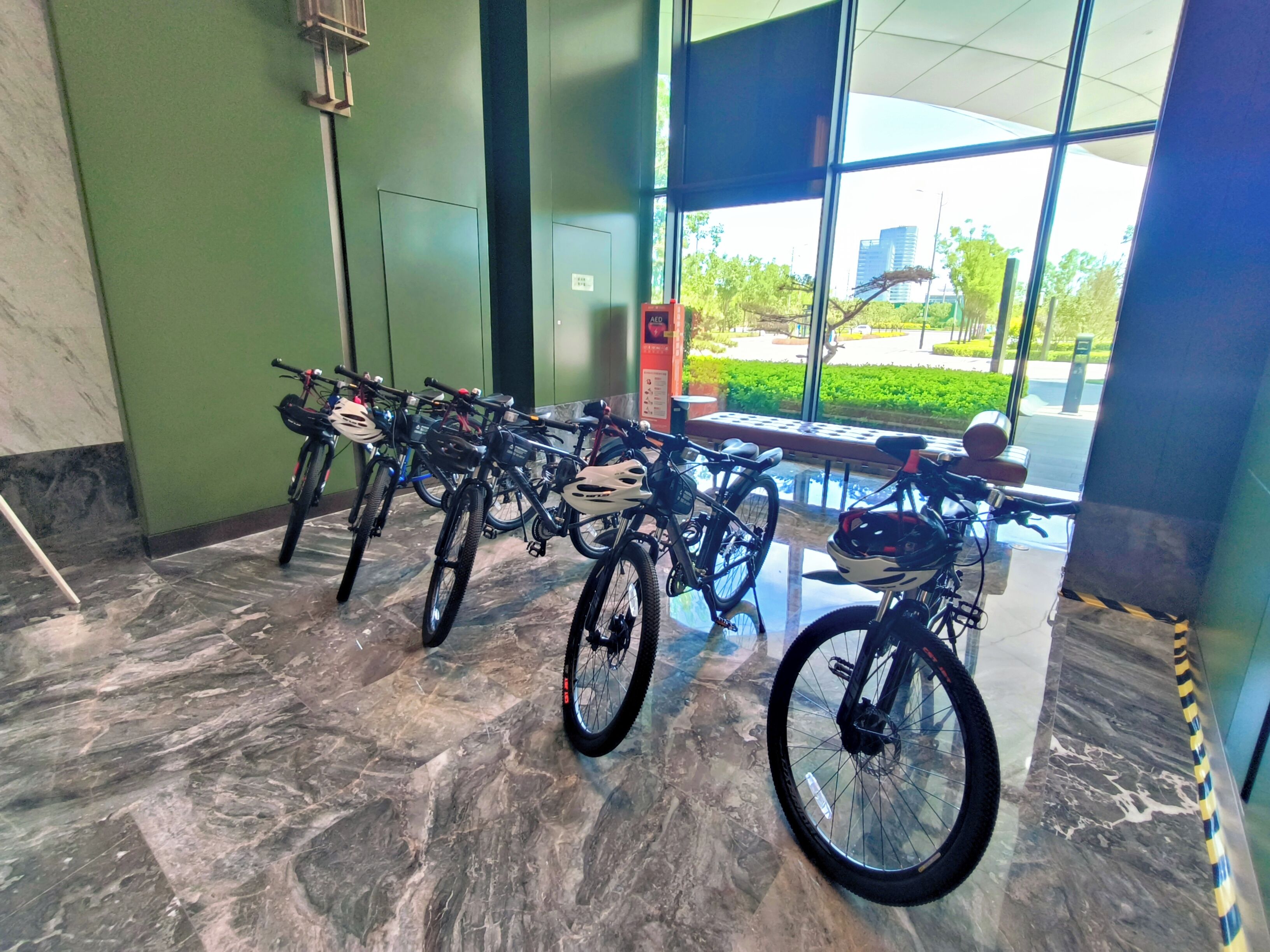 A row of bicycles parked indoors with a view of a cityscape through large windows.