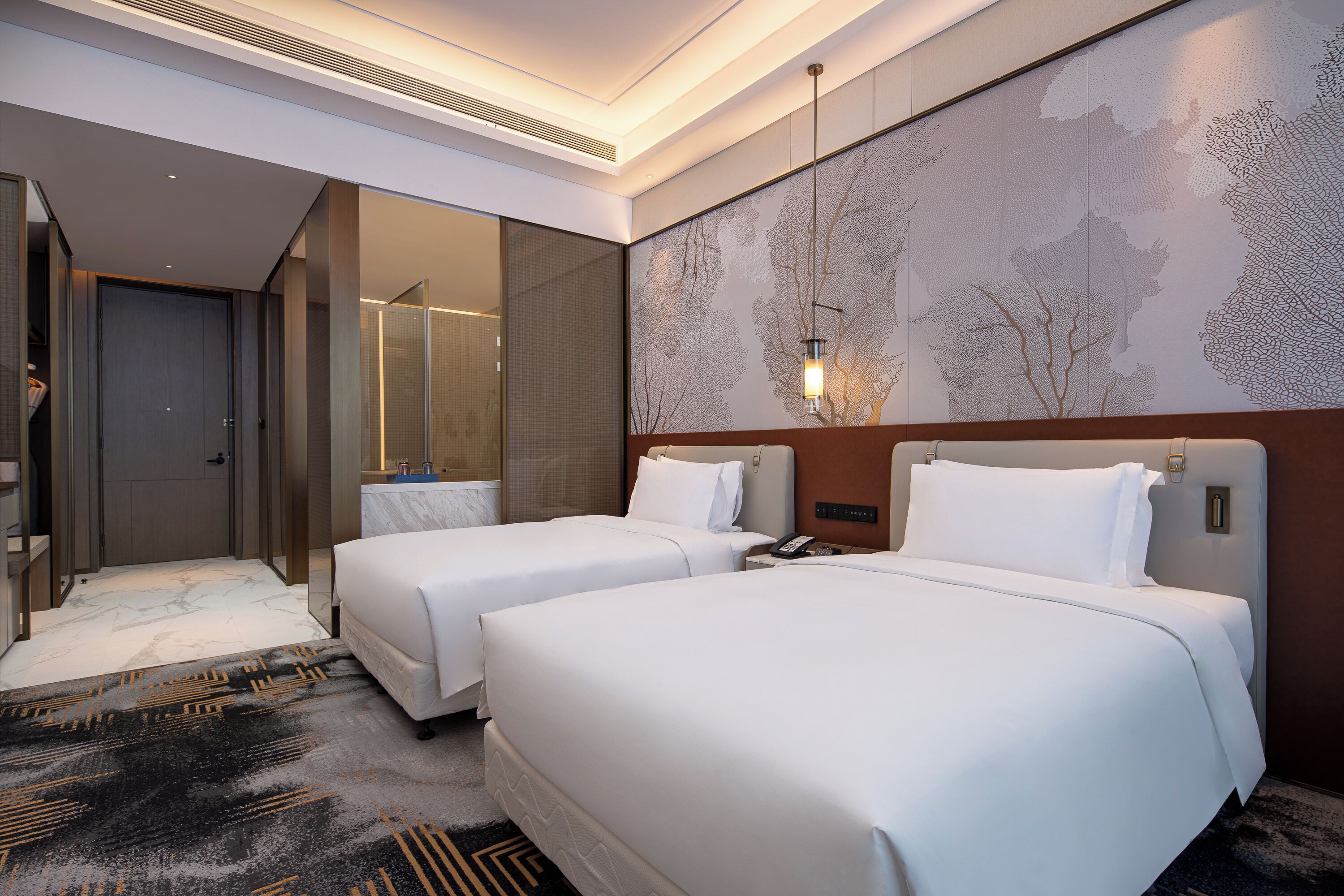 Une chambre d’hôtel avec deux lits, un grand miroir, une lampe fixée au mur et un sol recouvert de moquette.
