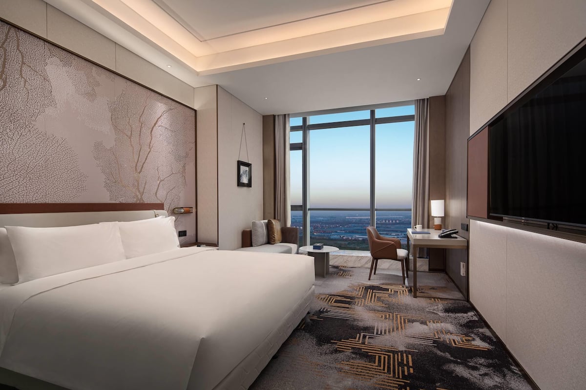 Habitación de hotel con una cama grande, un escritorio, una silla y vista a la ciudad.