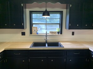 A kitchen with dark cabinets, a black pendant light, a window with a view, and a 'Home sweet home' sign. - Private Country Home- 15 mins from Moultrie/Adel (Moultrie)