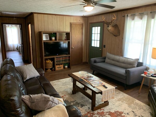 A living room with a brown leather couch, a grey sofa, a wooden entertainment unit with a TV, and a deer head mounted on the wall. - Private Country Home- 15 mins from Moultrie/Adel (Moultrie)