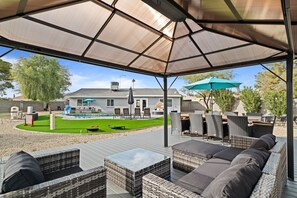 Une terrasse extérieure avec des meubles en osier, une piscine et un espace abrité.