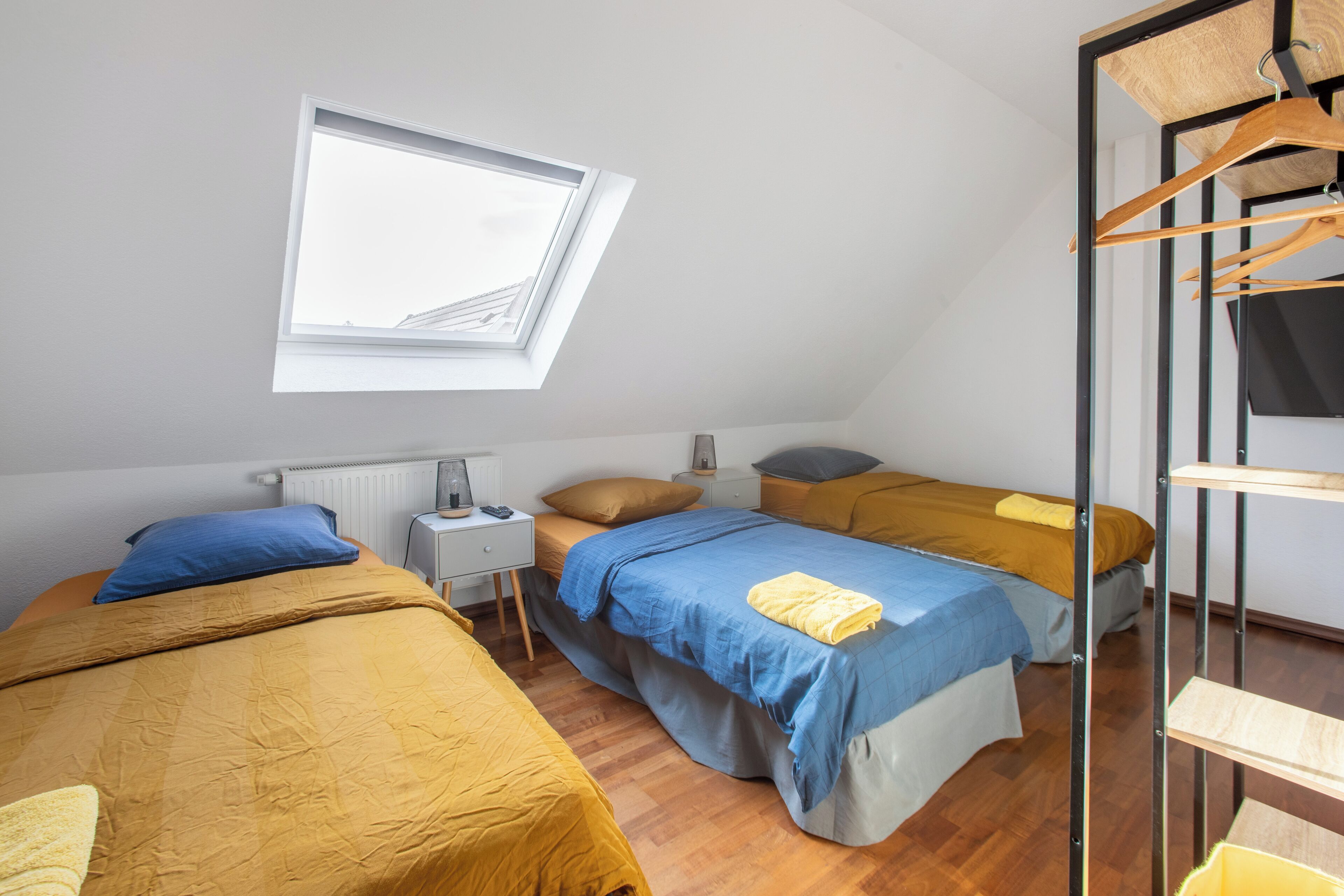 Un dormitorio con dos camas, tragaluz, radiador, mesita de noche y perchero.