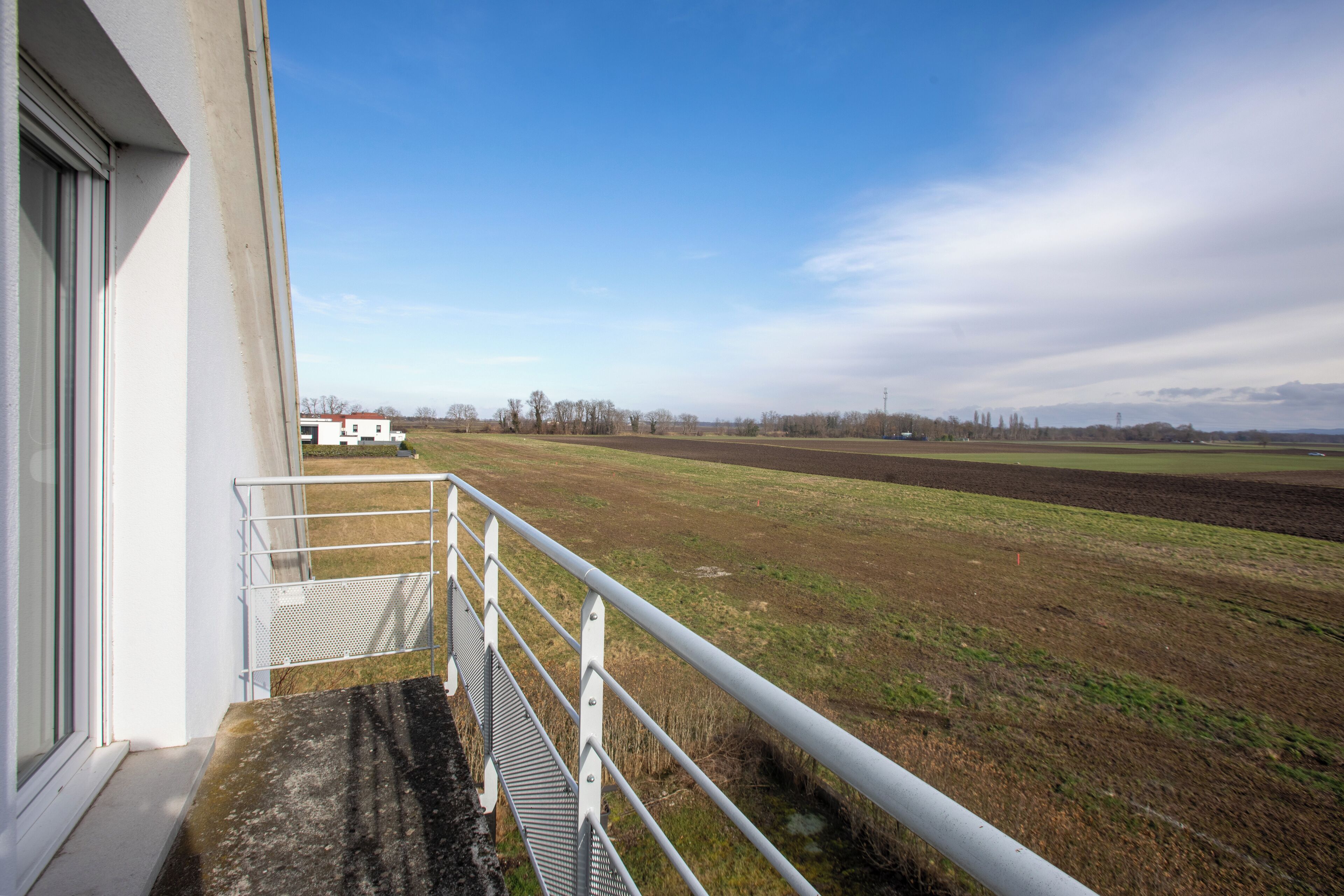 Ein Balkon mit Metallgeländer und Blick auf ein Feld.
