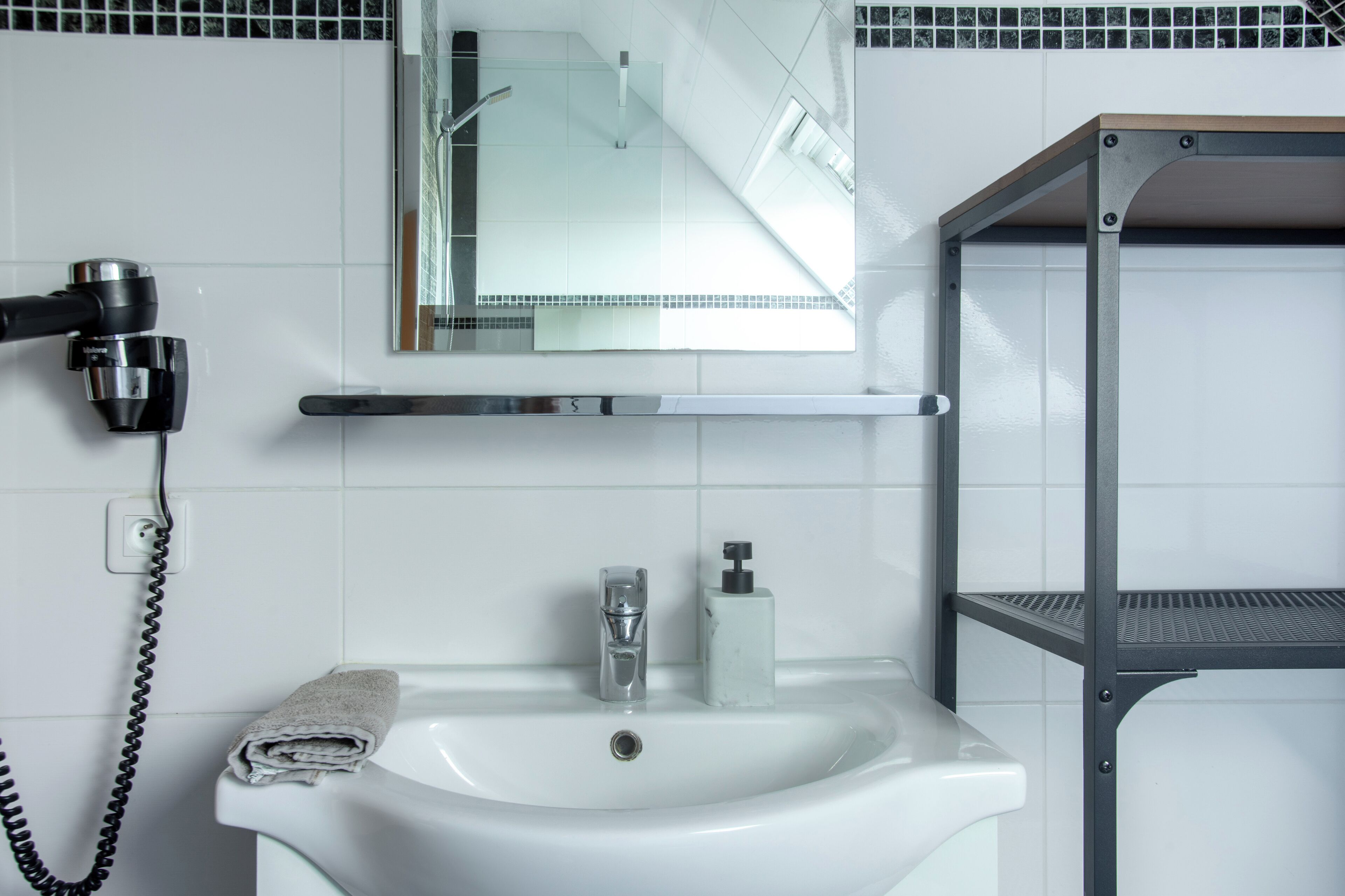 A bathroom with a white sink, a mirror, a towel, a hairdryer, and a shelf.