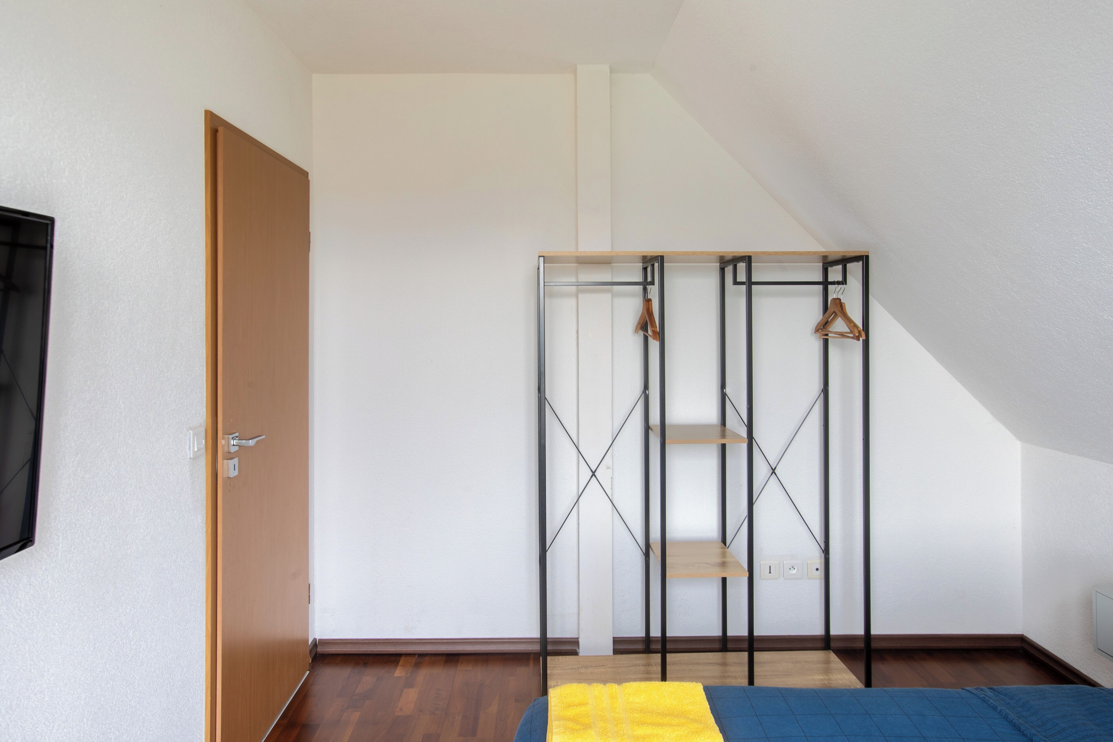 A room with a bed, a wooden door, a metal wardrobe, and a white wall.