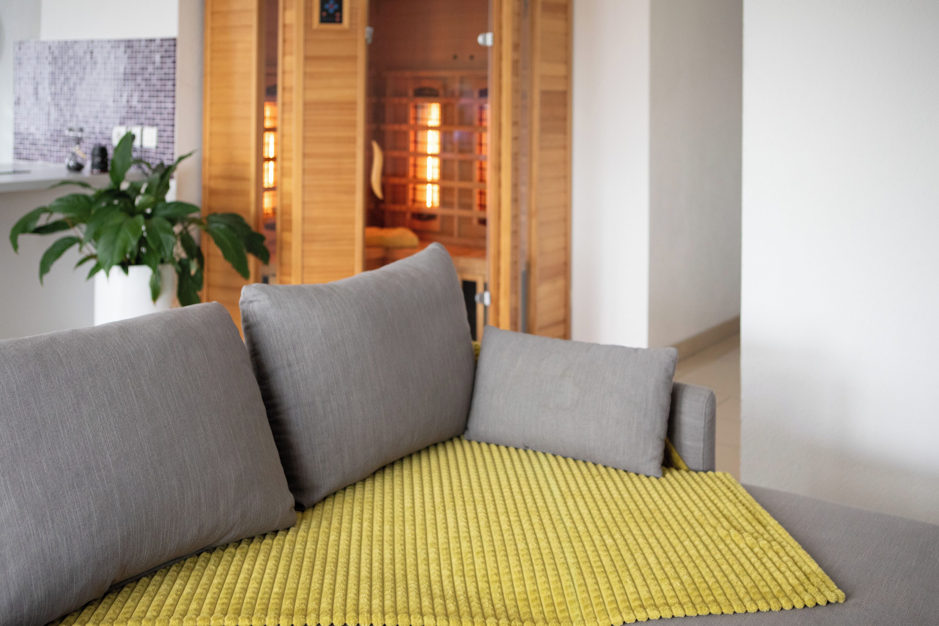 A modern living room with a grey sofa, a yellow textured throw, and a potted plant.