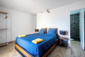 Een moderne slaapkamer met een groot bed, twee nachtkastjes met lampen, een kledingkast, en een douchecel zichtbaar achter een glazen deur.