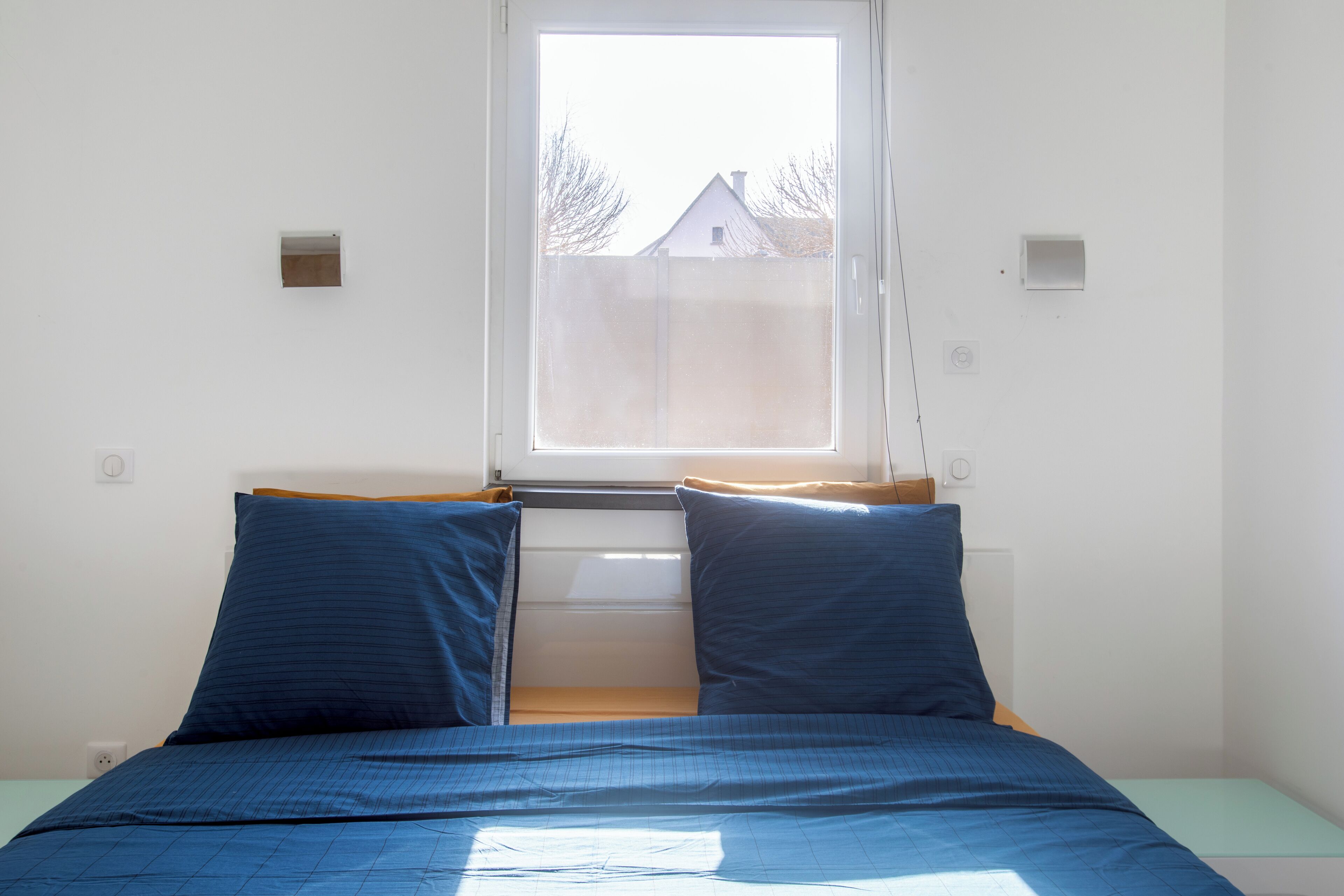 Un dormitorio con cama, ventana y vista a una casa.