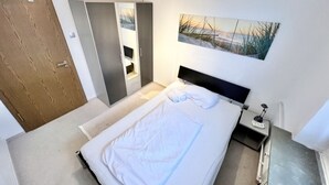 Een slaapkamer met een bed, nachtkastje, schilderij en een deur.