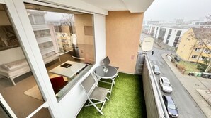 Een balkon met een kleine tafel en stoelen, uitzicht op de straat hieronder, en een gebouw op de achtergrond.