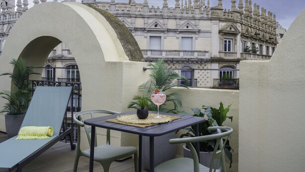 Una terraza en la azotea con una mesa, sillas y una tumbona.
