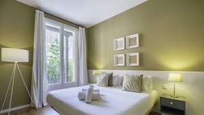 Habitación de hotel con una cama grande, dos mesitas de noche con lámparas, una lámpara de pie, una ventana con cortinas y decoración en la pared.