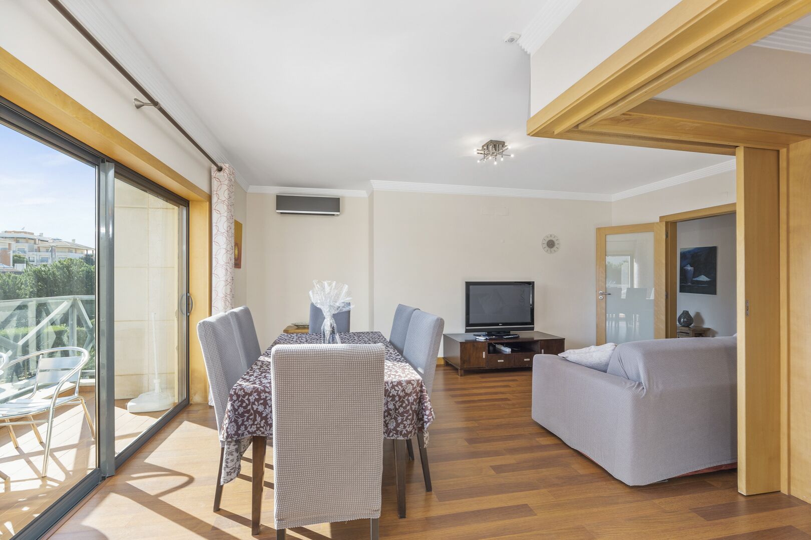 A modern living room with a dining area, a television, and a balcony with glass doors.