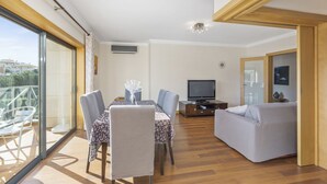 Ein modernes Wohnzimmer mit Essbereich, einem Fernseher und einem Balkon mit Glastüren.