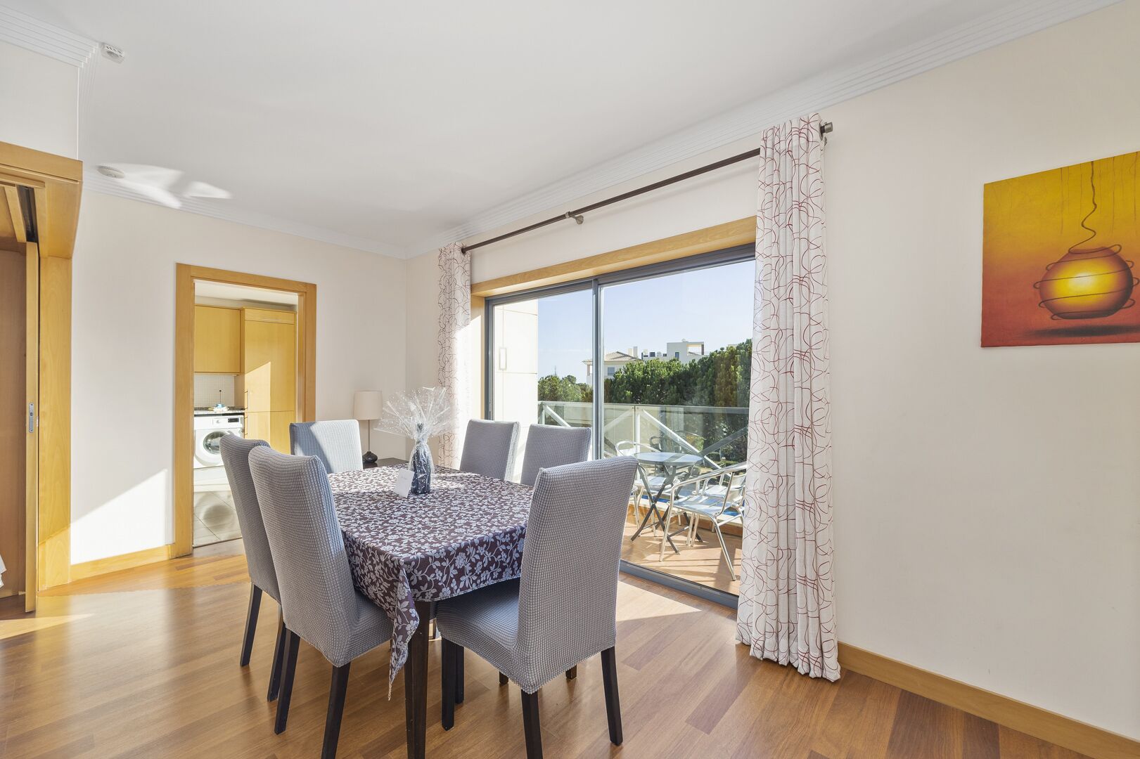 A dining area with a table set for four, a large window with a view, and a balcony with outdoor furniture.