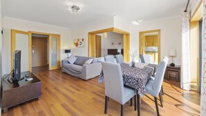Ein modernes Wohnzimmer mit einer Couch, einem Esstisch, Stühlen, Holzboden und einem Fernseher.