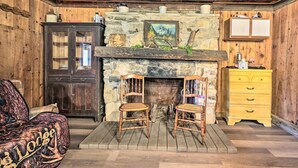 Una habitación rústica con chimenea de piedra, muebles de madera y un aparador amarillo.