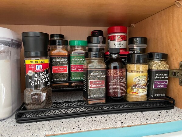 A spice rack with various spices and seasonings, including black pepper grinder, red pepper, organic crushed red pepper, ground cinnamon, pure bourbon vanilla extract, and 21 seasoning salute.