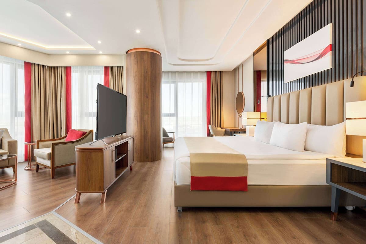 A modern hotel room with a large bed, a flat-screen TV, a desk, and a seating area.