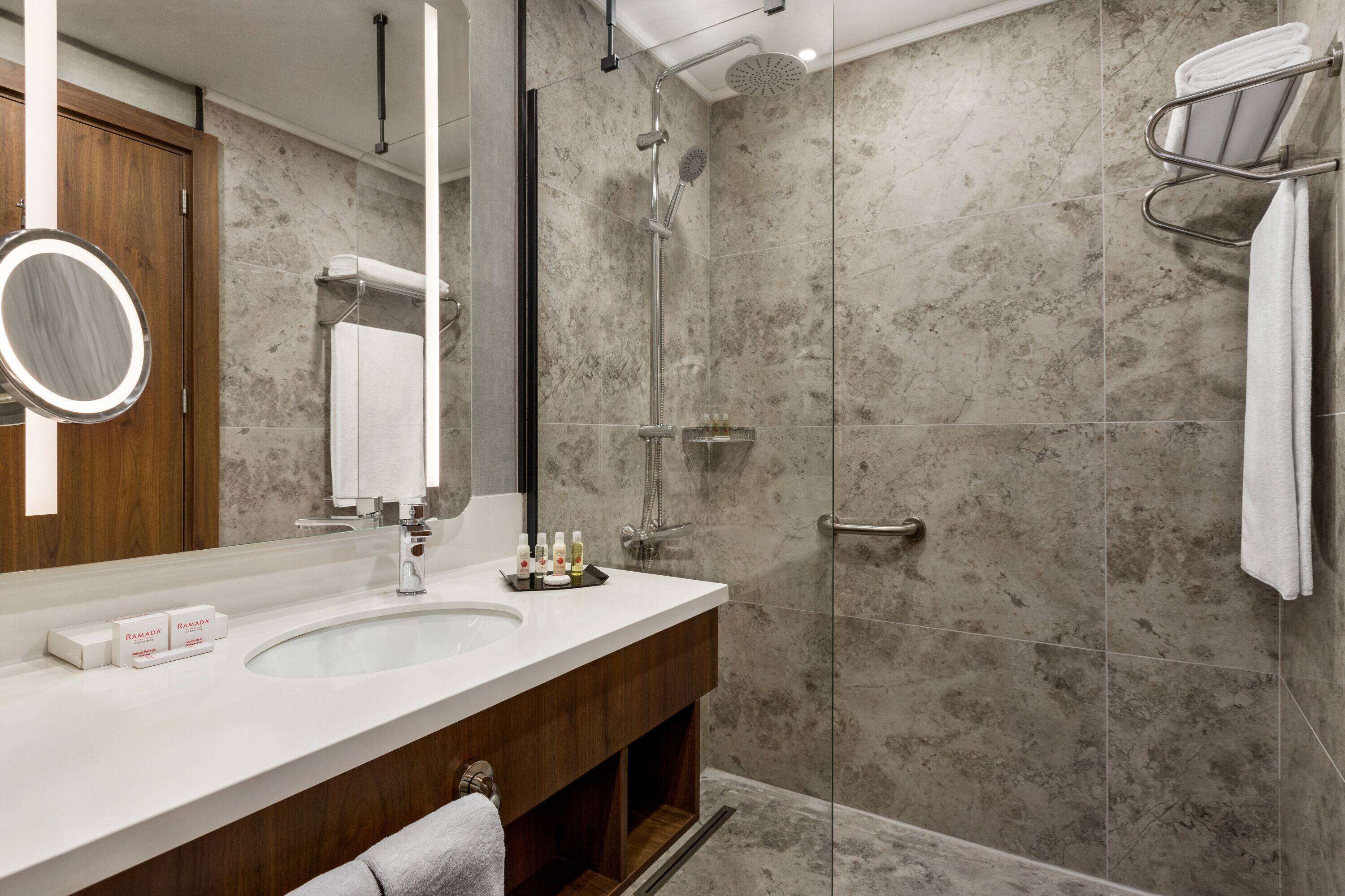 Un baño moderno con ducha de mármol, tocador de madera y un espejo grande.