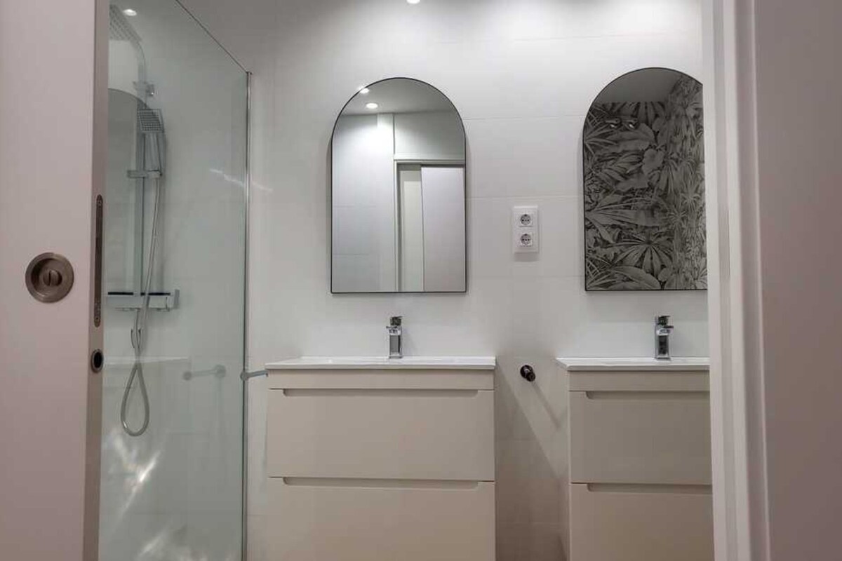 Ein Badezimmer mit zwei Waschbecken, einer Duschkabine aus Glas und einem wandmontierten Spiegel.