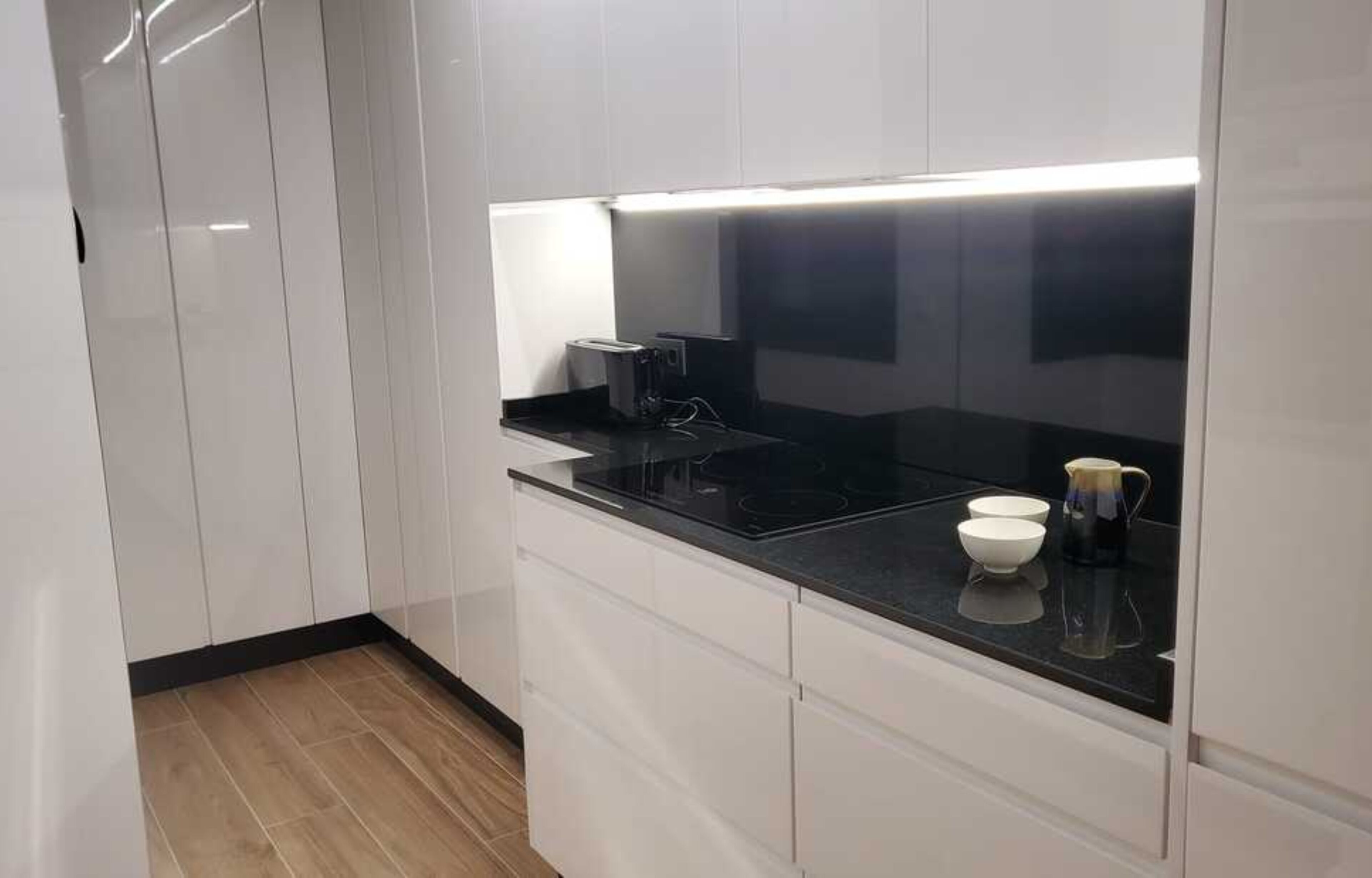 Una cucina moderna con mobili bianchi, un piano di lavoro nero e un piano cottura integrato.