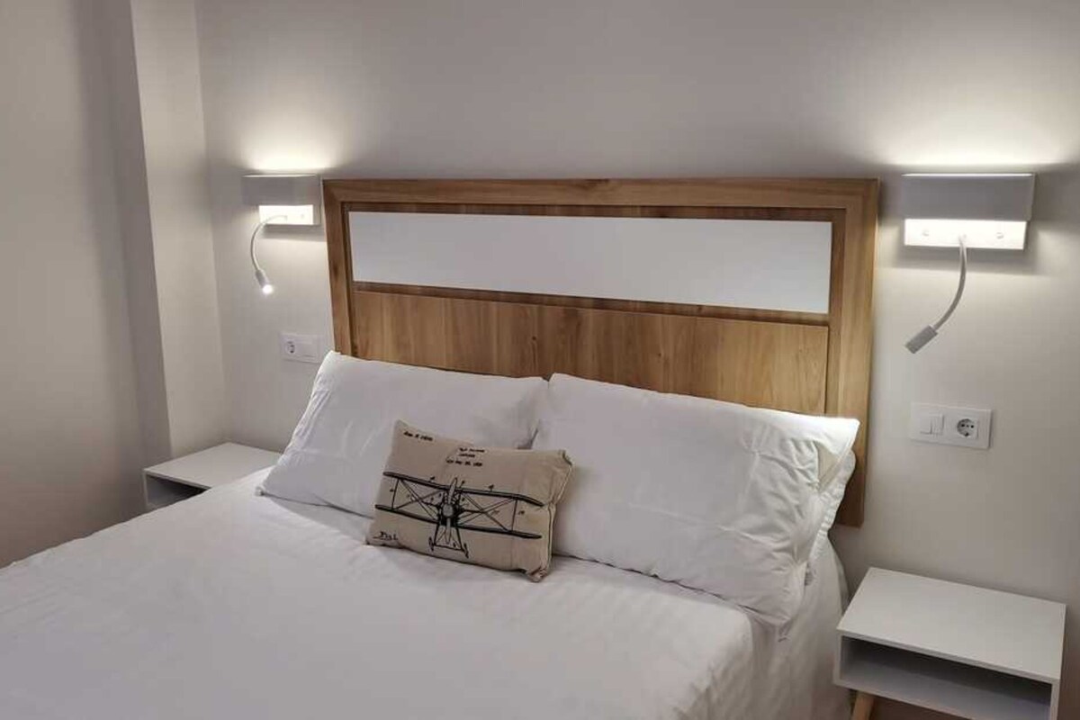 Une chambre d’hôtel avec une tête de lit en bois, du linge de lit blanc et deux lampes de chevet.
