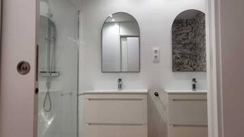 A modern bathroom with a glass shower enclosure, two sinks, and a decorative mirror with an arch design.