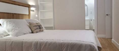 Un dormitorio con una cama grande, cabecera de madera, unidad estantería empotrada y una puerta que da al baño.
