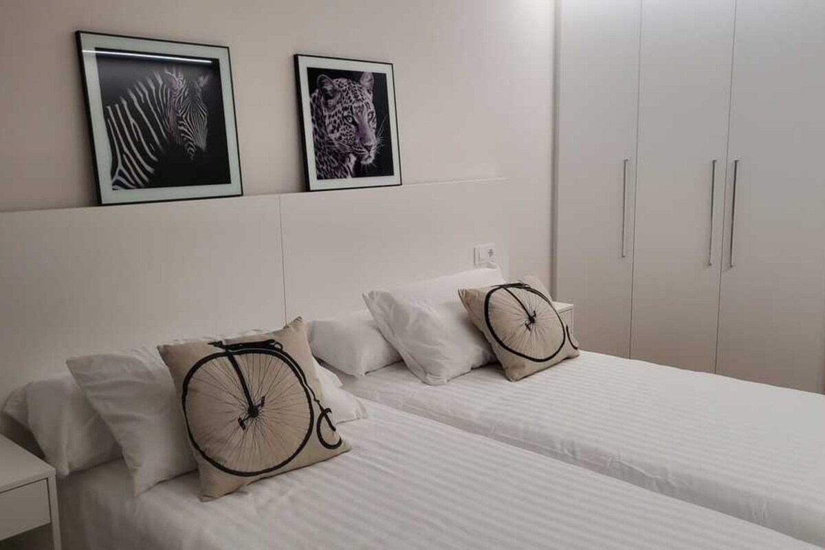 Ein Hotelzimmer mit zwei Betten, weißer Bettwäsche und einem an Kunstwerken verzierten Kopfteil.