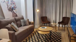 Ein modernes Wohnzimmer mit einem braunen Sofa, zwei Sesseln, einem Couchtisch, einem Fernseher und einem Gemälde an der Wand.