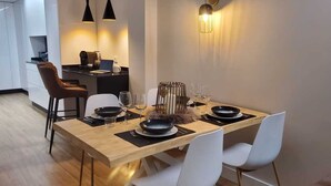 Ein moderner Essbereich mit einem Holztisch, gedeckt für vier Personen, weißen Stühlen und einer Küche im Hintergrund.