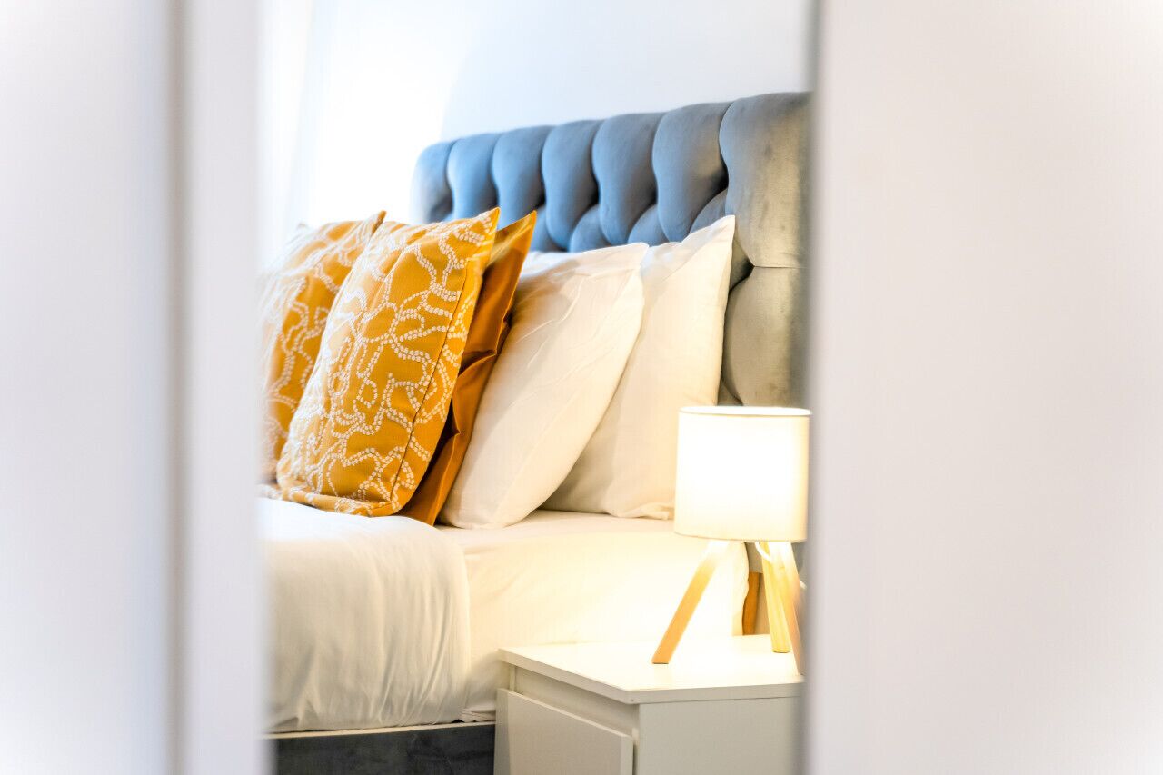 A neatly made bed with a tufted headboard, a bedside lamp, and patterned pillows.