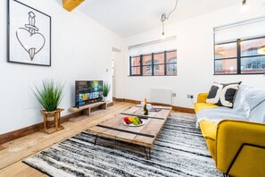 A modern living room with a wooden coffee table, a yellow sofa, and a television displaying 'HOBBIT'.