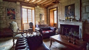 Una habitación rústica con paredes de piedra, vigas de madera, chimenea, sofás de cuero y muebles antiguos.