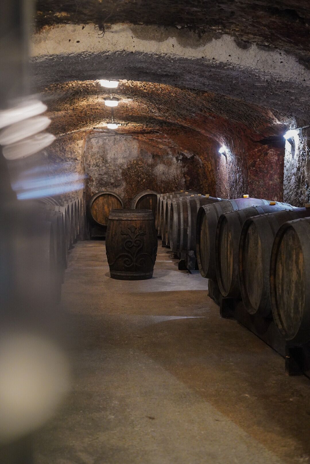 A dimly lit cellar with rows of wooden barrels and a large barrel with intricate carvings.