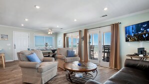 A spacious living room with a wooden floor, a ceiling fan, and a large window overlooking a balcony. - Just Beachy: Beachfront, Private pool, Pet Freindly (St. George Island)