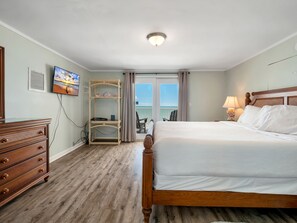 A hotel room with a wooden bed, a dresser, a TV, a shelf with decorative items, and a view of the outdoors through the window.