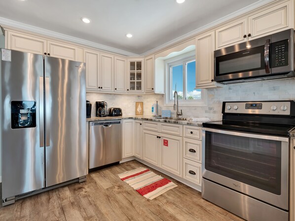 A modern kitchen with stainless steel appliances, white cabinetry, and a wooden floor.