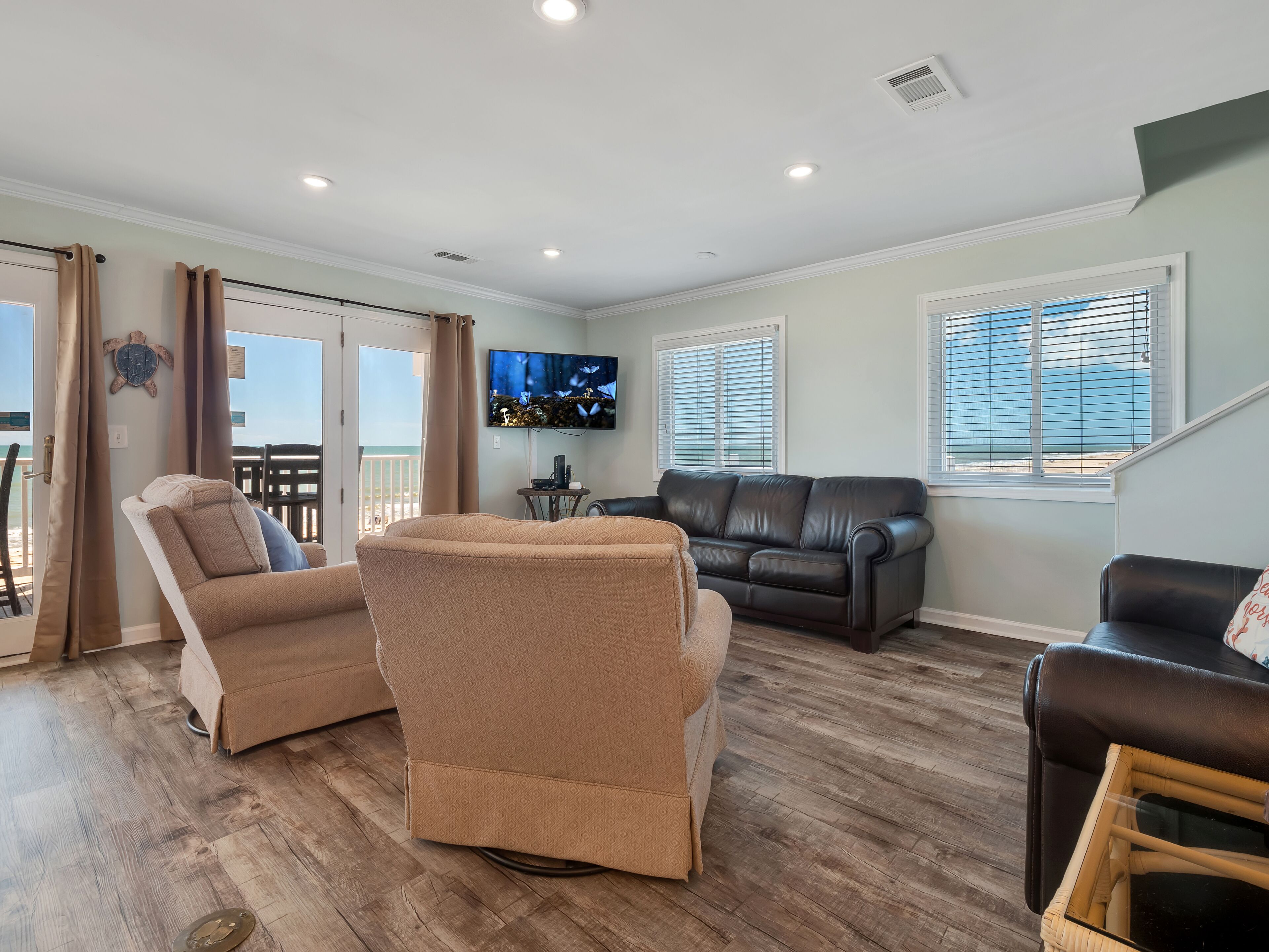 A living room with a sofa, armchairs, a television, and a balcony with curtains.